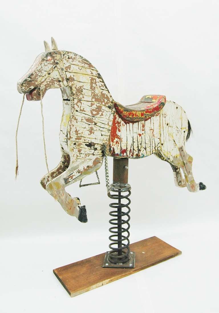 An antique wooden carousel horse converted to a rocking horse with a spring on a wood base. The paint on the horse, last painted in a brown color, is chipping exposing some of the natural wood and the colors painted before. The horse has marbles for