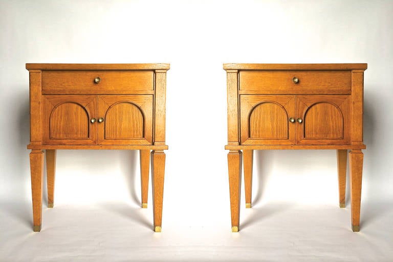 Two fine oak bedside tables featuring a drawer and a two-door cabinet for storage. Each piece has three small pulls and leg caps in gilt bronze. There is a Maker's plaque on the underside of each nightstand marked Decaux and Maous and includes the