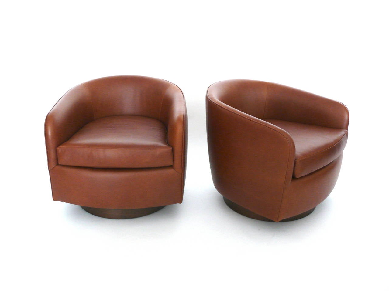 Handsome pair of swivel chairs in the style of Milo Baughman. Newly upholstered in saddle leather and resting on a medium walnut base. Extremely comfortable and classic design. Perfect for the home or office. Custom leather options also available.