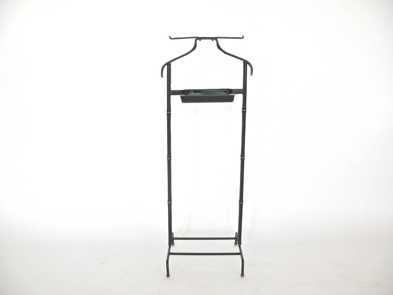 Handsome black leather valet by Jacques Adnet. Valet has coat rack and pant rack with signature contrast stitching. Valet sits atop brass ball feet. Small curved catch-all perfect for watch and cufflinks. Excellent vintage condition.