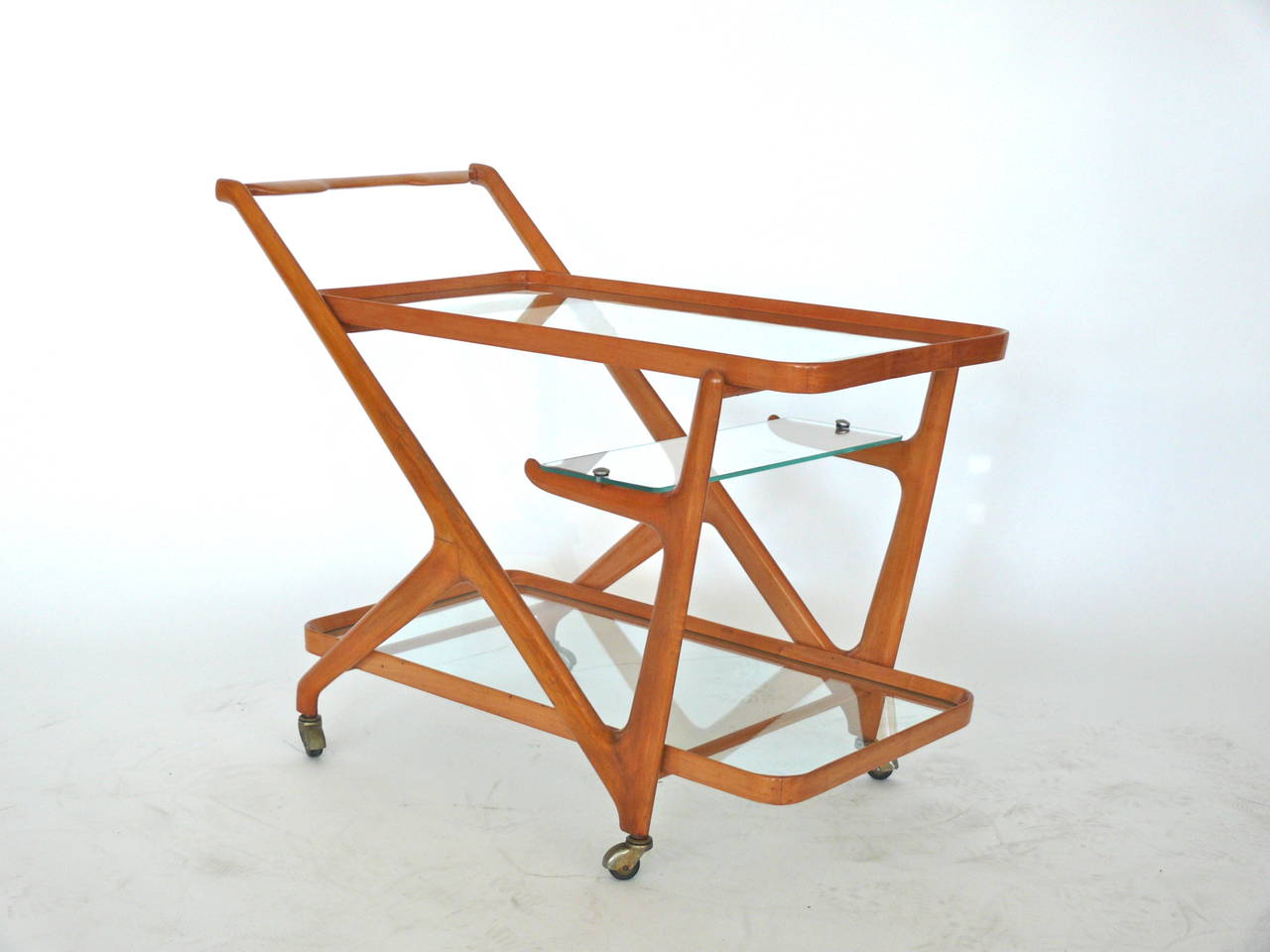 Italian Cesare Lacca rolling bar cart, manufactured by Cassina in the 1950’s. Wonderful organic sleek shape in a beautiful walnut with three glass shelves. Two large shelves on top and bottom with a small shelf floating in the middle. Original