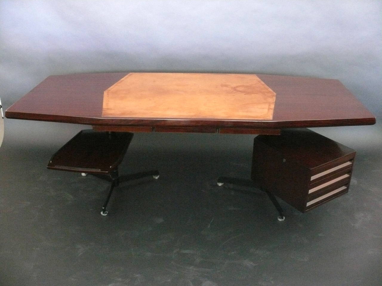 Handsome rosewood desk by Osvaldo Borsani. Pull-out tray table and set of drawers both revolve 360 degrees. Beautiful saddle leather inlaid desk blotter in original condition with great patina. The desk sits upon two tripod blackened nickel bases.