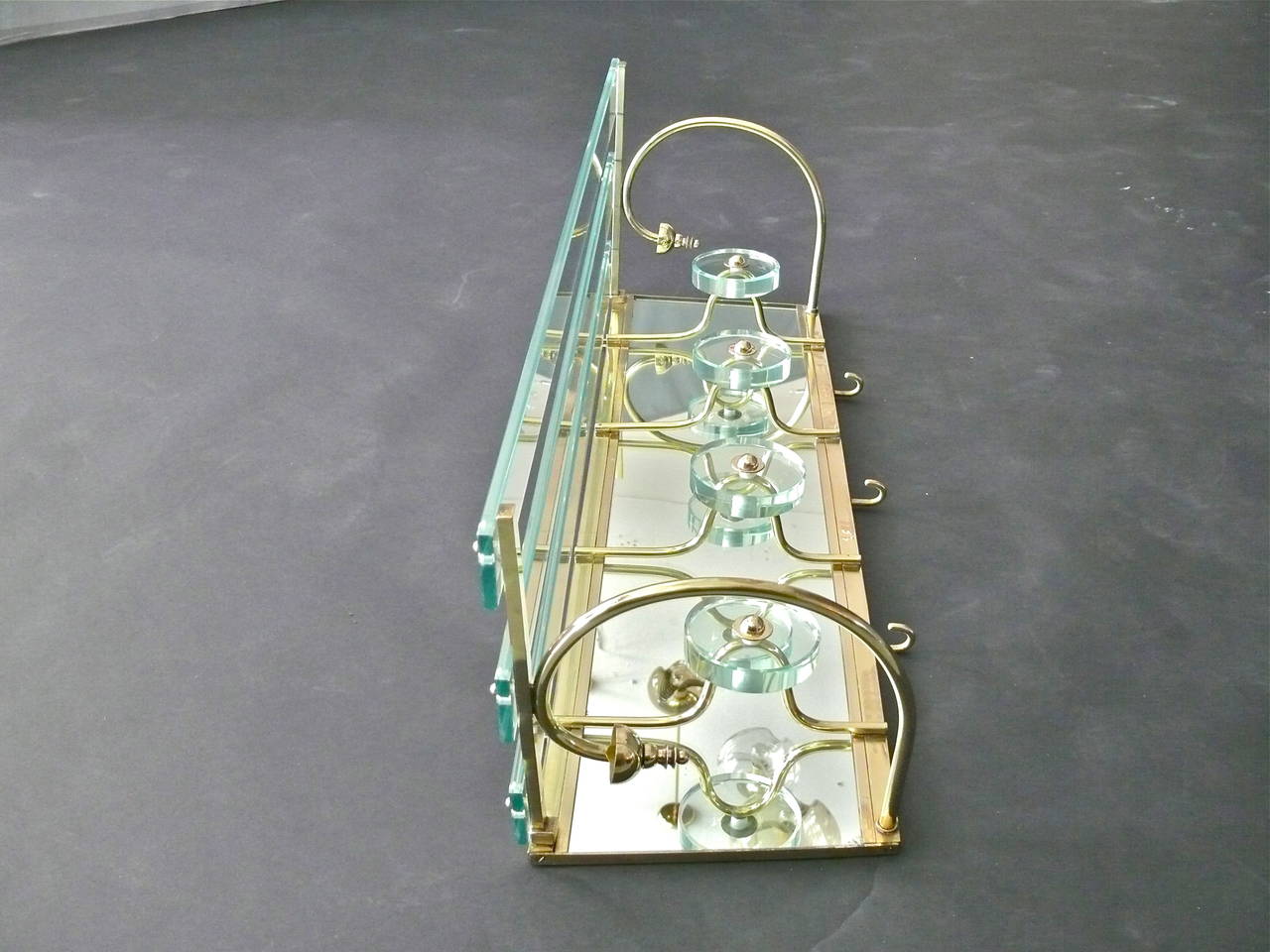 Beautiful Italian coat rack in the style of Fontana Arte. Made with four glass disc hooks, mirrored back, slated glass shelf and brass hardware with great patina. Three small brass hooks on underside of rack. Stunning design and rare find!