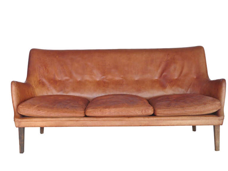 Amazing three seater leather sofa designed by Arne Vodder for Ivan Schlecter.  Upholstered in original rust colored leather with incredible patina and character. Unique shape with intriguing curves and lines. Sofa rests on original oak tapered legs.