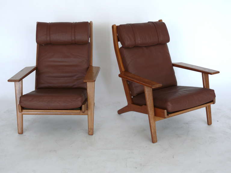 Wonderful pair of oak and leather highback armchairs by Hans Wegner. Original leather and wood have great patina. Leather head-rest slides in through two straps. Wide arms and deep seat. Extremely comfortable!