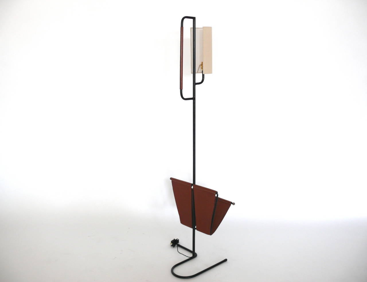 Fantastic floor lamp with built-in magazine rack by Jacques Adnet. Iron frame with saddle leather magazine holder. Iron bar closest to shade is also wrapped in saddle leather. New silk shade. Newly rewired. Very unique piece.