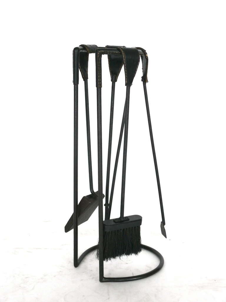 Handsome Jacques Adnet fireplace tool set. Tools are fully covered in original black leather with white contrast stitching and rest on black iron stand. Great patina on individual pieces. Set includes includes poker, log grabber, broom and shovel.