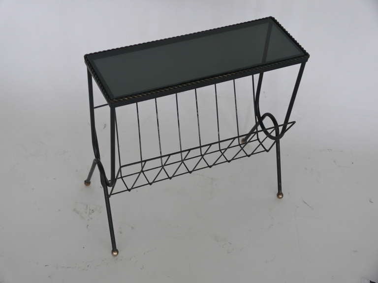 Great French side table and magazine rack. Black glass top with black iron frame. Iron twist detail around glass surface and brass ball feet detailing. Great patina and chipping to paint consistent with age. Unique accent piece for any room.