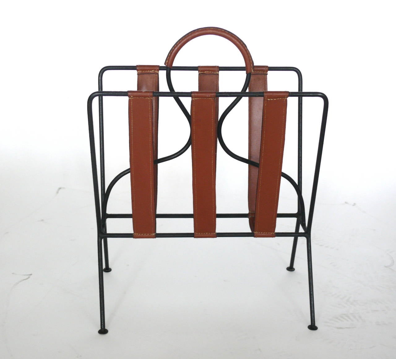 Handsome magazine rack by Jacques Adnet. Iron frame with saddle leather straps and leather wrapped handle. Signature contrast stitching throughout. Great patina to leather. Excellent vintage condition.