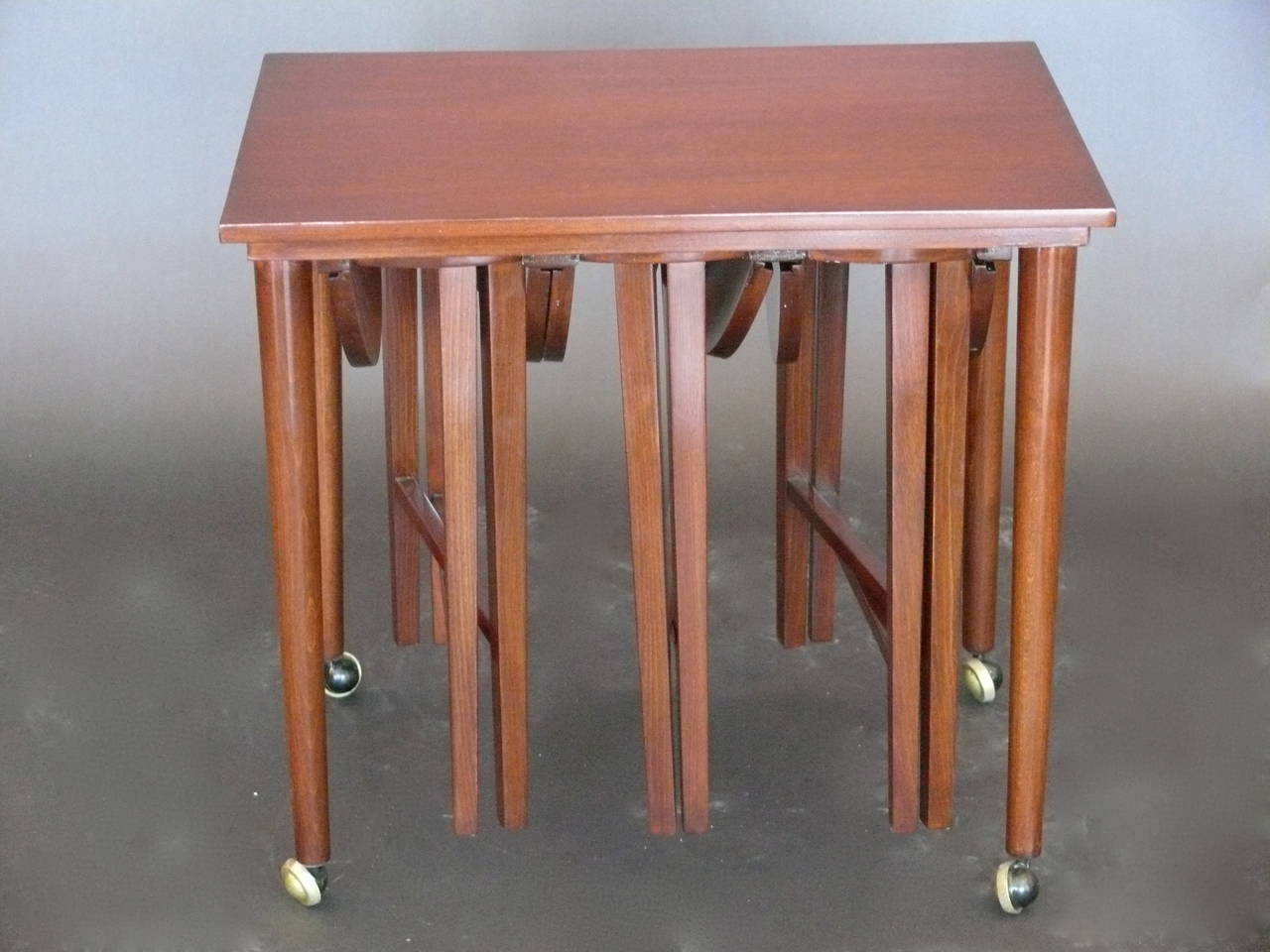Fantastic end table on original brass casters. End table houses three round, drop-leaf tables. Newly refinished in a rich polished walnut. Very functional piece. Great for entertaining.
