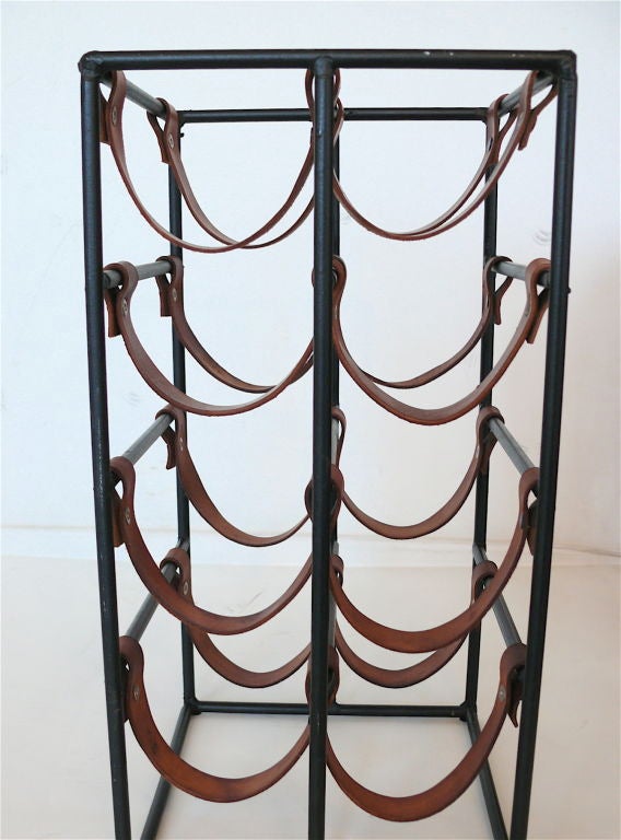 Classic Paul McCobb wine rack in black iron and original leather, the leather straps with fine patina and black rivets. Small and functional, holding eight bottles of wine.