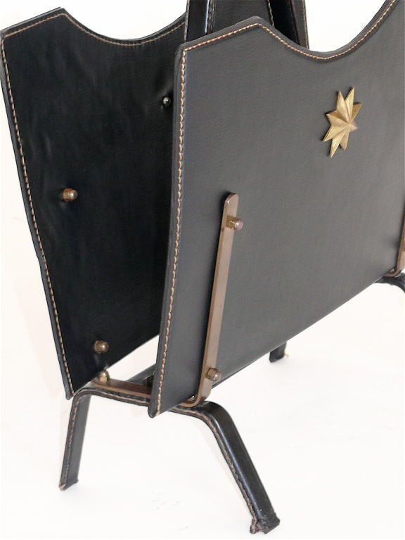 Handsome Jacques Adnet black skai magazine rack with brass detailing, a brass hoop handle and a gold polygon star.