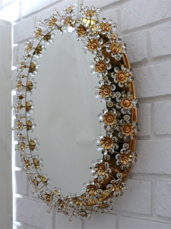 Stunning oval Italian backlit mirror with two rows of cut crystal balls and flowers with brass centers attached to curved outstretched brass arms. Light illuminates through flowers to create a beautiful glow. Professionally re-wired. Three available
