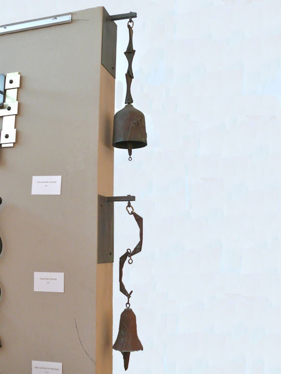 One iron bell wind chime designed by Paolo Soleri. The bell is suspended from an iron wall plate on a shaped stem. The 
