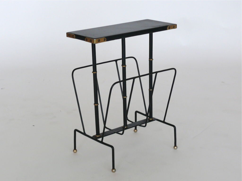 Jacques Adnet side table and magazine rack. The skai leather top with brass corners rests on three iron and brass bamboo supports. The magazine rack is attached at the base and terminates in brass ball feet.