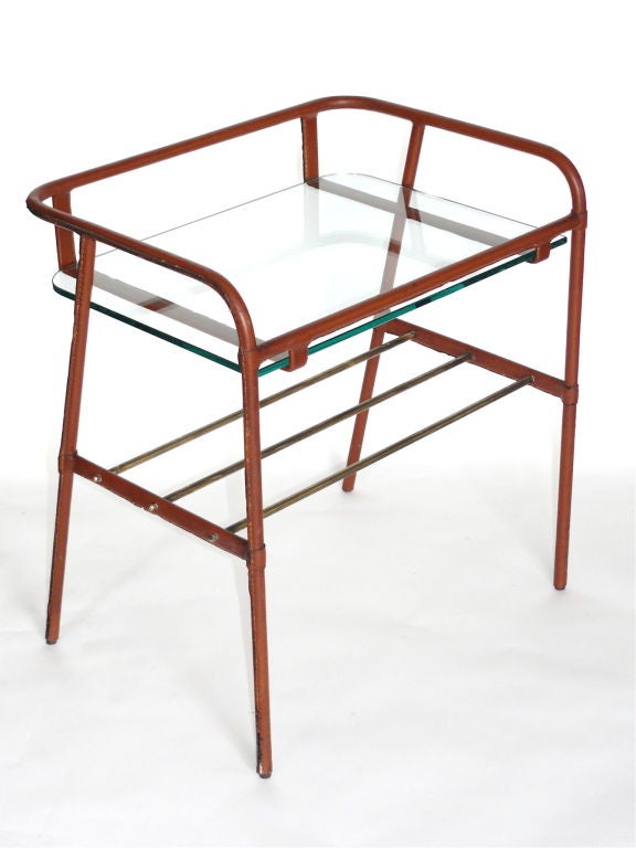 Handsome angular end table by Jacques Adnet, the wrapped brown leather frame holding a clear glass top shelf and open brass middle shelf. Beautiful original leather.