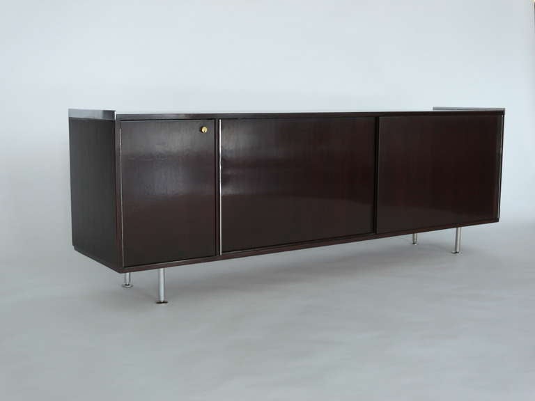 Gorgeous long credenza from Italy. Newly refinished dark mahogany wood and steel legs and edge detailing. Sliding front door with steel handle exposes open shelving. Single small door with lock and key. Sleek and modern design - beautiful piece for