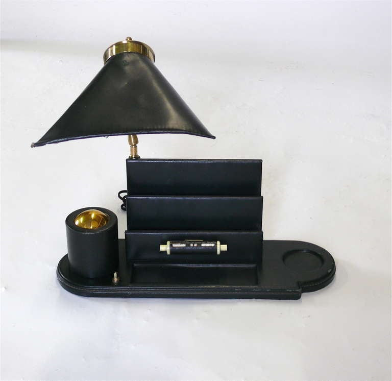 Rare Jacques Adnet desk caddy. Fully covered in original dark hunter green leather with brass detailing. Letter holder, adjustable lamp, swivel brass cigarette holder, built in calendar, and pen tray. Great patina and distress leather.