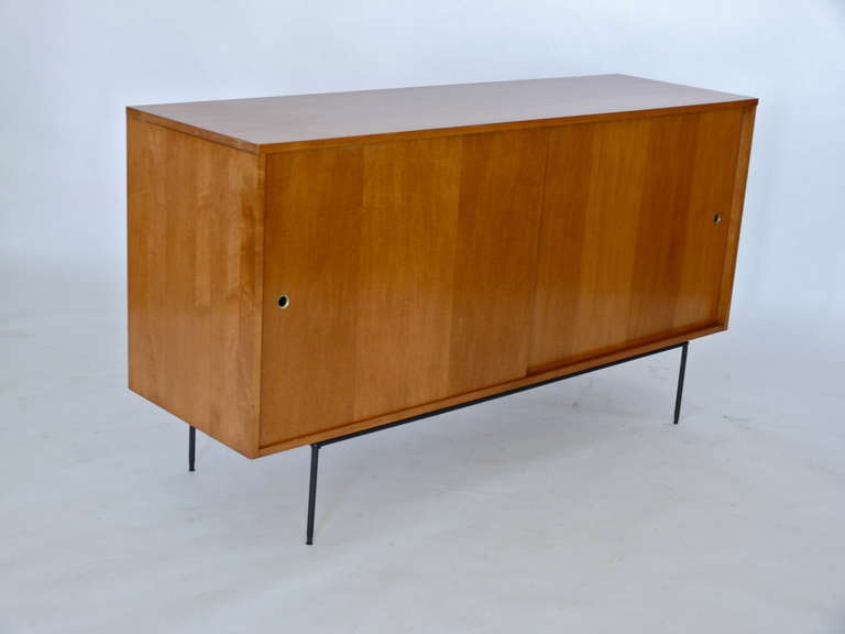 Simple and sleek sideboard designed by Paul McCobb for Planner Group. Walnut wood cabinet rests on slender iron straight leg base. Doors with brass hardware slide open to reveal shelfs and drawers for storage. Fantastic mid-century modern piece.