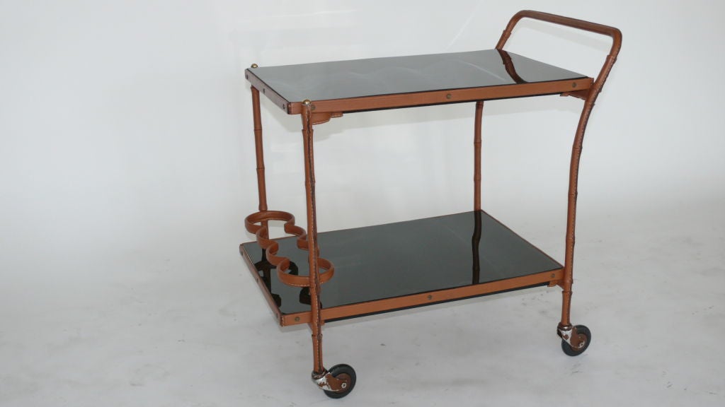 Stunning Jacques Adnet bar cart wrapped in rich carmel leather with signature contrast stitching on bamboo legs. Two shelves are in skai leather, black glass tops, and original casters.