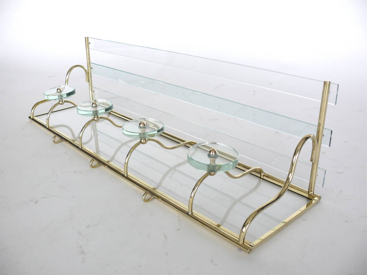 Fantastic Italian coat rack in the style of Fontana Arte. Made with four glass disc hooks, mirrored back, slated glass shelf and brass hardware with great patina. Three small brass hooks on underside of rack. Very similar rack also available.