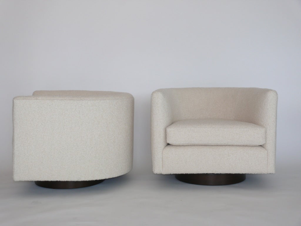 Fantastic pair of swivel chairs with stained walnut wood bases in the style of Milo Baughman. Newly reupholstered in a creamy white wool boucle fabric. Extremely comfortable and functional with sleek modern design.