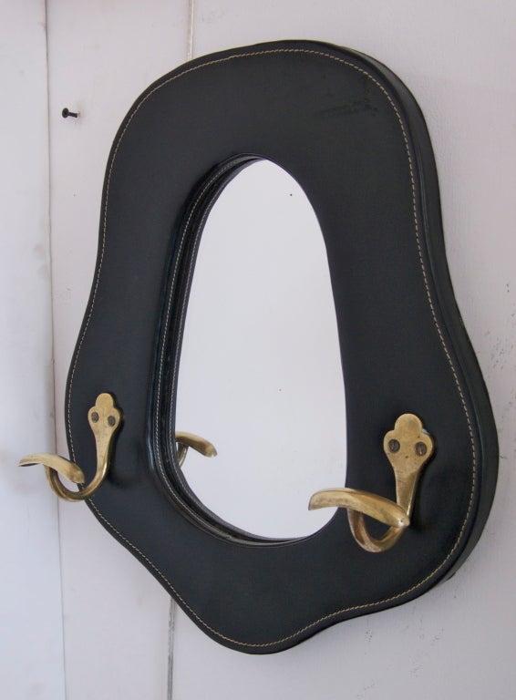 Beautiful black leather mirror by Jacques Adnet with signature contrast stitch detailing around edge. Nice curvy oval shape with two solid brass hooks. Lovely piece.
