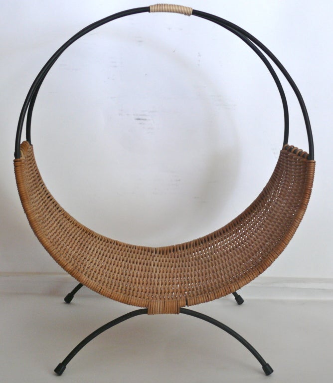 Fantastic French log or magazine holder made of black iron frame and woven wicker. Circular iron frame rests on 2 arched iron legs. Nice woven wicker detail handle. Beautiful piece to display logs by a fireplace or to hold magazines.