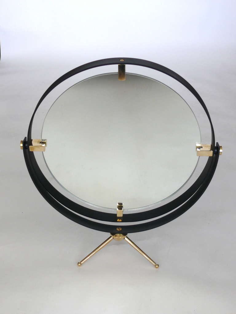 Fantastic iron frame with polished brass clasps support the floating circular mirror.  Stands on a brass tripod base and tilts to your liking. 

Made in Los Angeles 