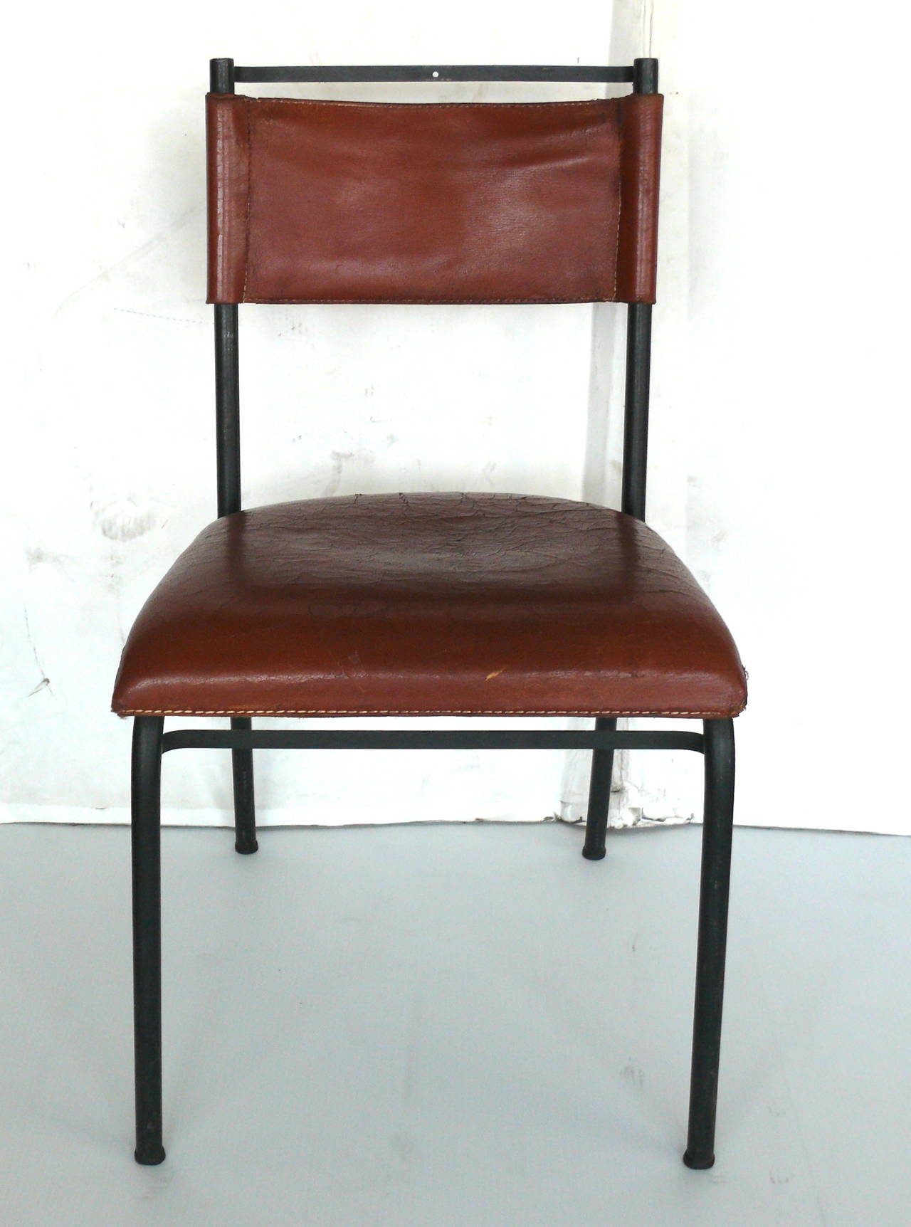 Handsome pair of leather and iron chairs by Jacques Adnet. Sturdy iron frame with cognac leather seat and back rest. Beautiful age and patina to leather. Characteristic Adnet contrast stitching throughout. Both chairs in their own state of vintage