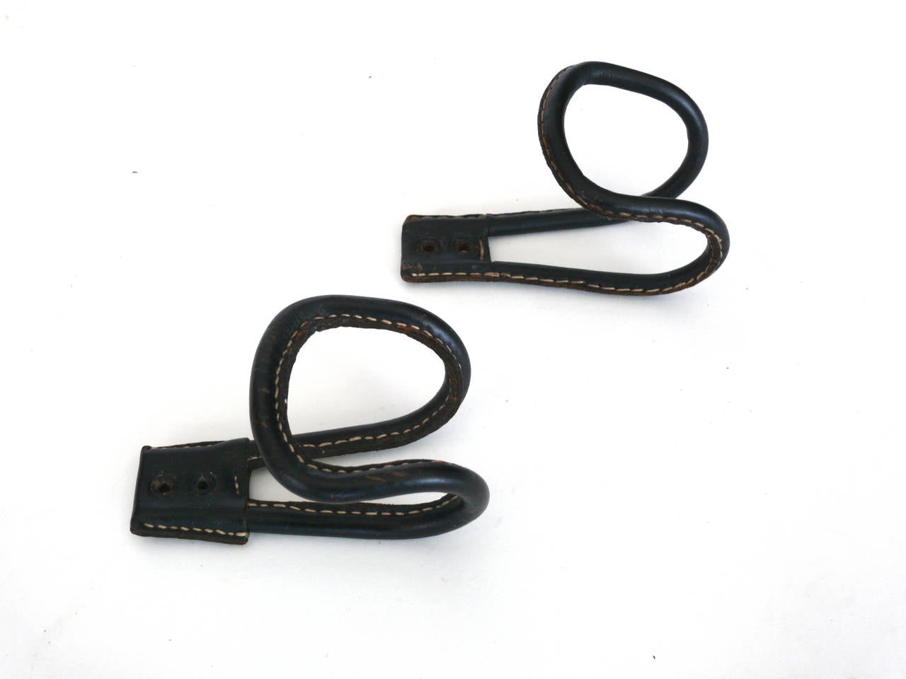 Single black leather coat hooks by Jacques Adnet with signature contrast stitching on black iron loop. Two available.
