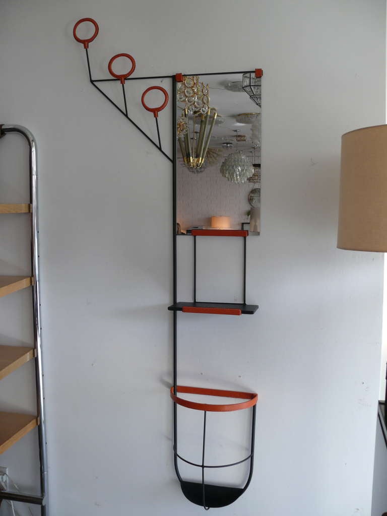 Beautiful newly produced leather and iron wall rack in the style of Jacques Adnet. Wall piece comprised of small mirror, three coat hooks, small flat catchall and umbrella holder - allowing for great function and storage. Gorgeous orange leather