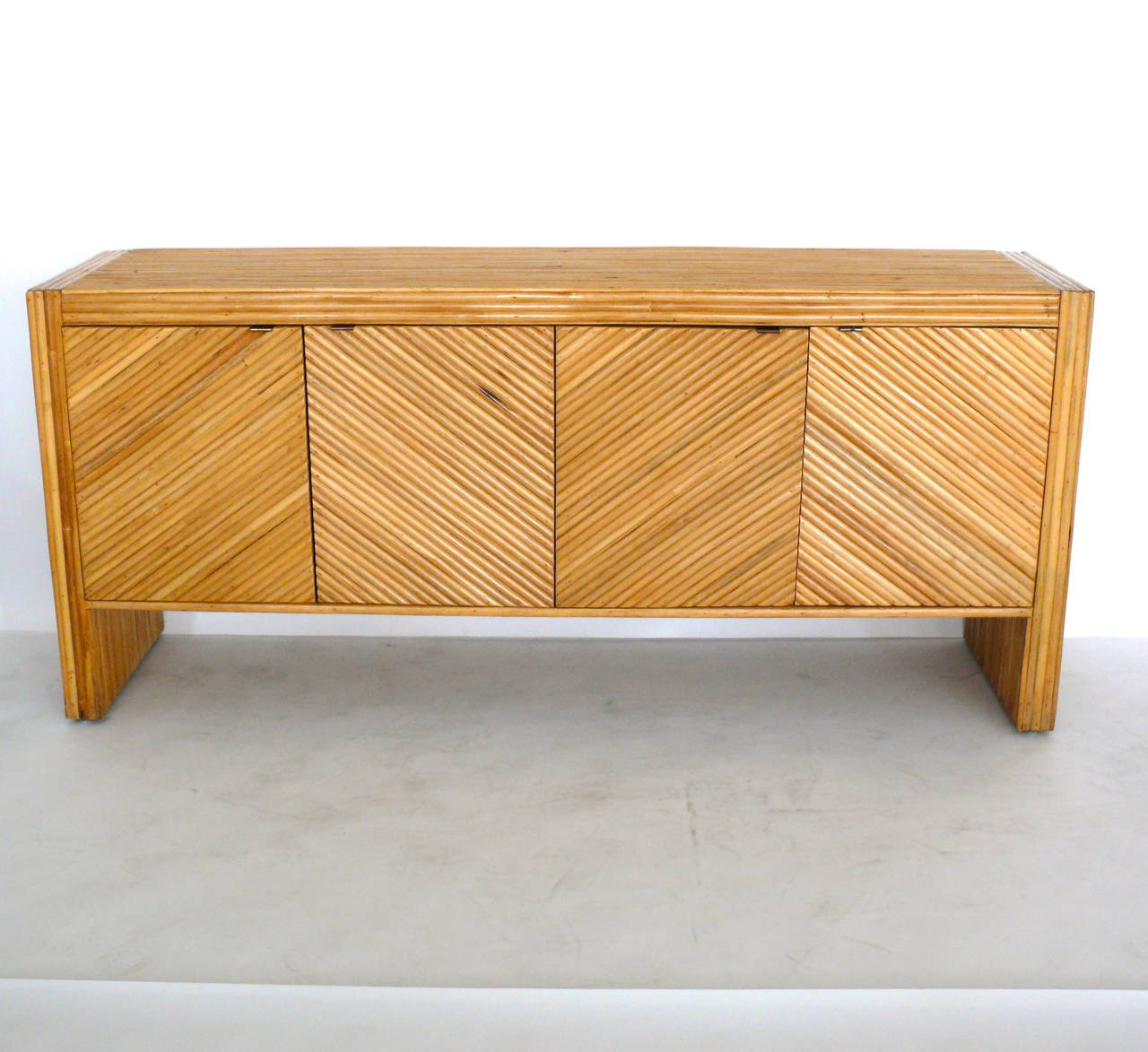Excellent sideboard in the style of Milo Baughman. Diagonal strips of rattan adorn the front of dresser with horizontal strips along the body. Doors have metal pulls with four total shelves inside. Very functional for the home or office. Excellent