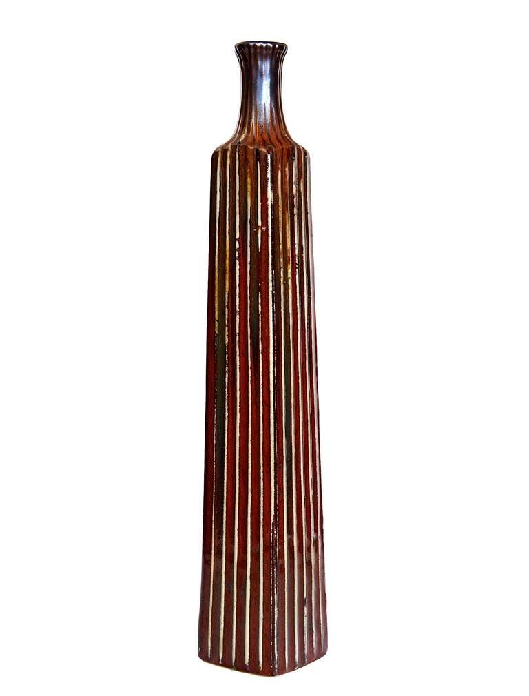 This attenuated bottle-form vase is stoneware, less commonly seen in Italy where earthenware was generally favored for its accomodation of brightly-colored and carefully controlled glaze effects. The striated relief decoration creates furrows for