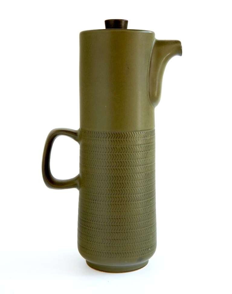 In its attenuated, cylindrical form, exquisite detailing of its spout and handle, and impressed surface decoration, Gill Pemberton's sage green coffee pot is a kind of summation of the state of taste in the early 1960s. Made by Joseph Bourne & Son,