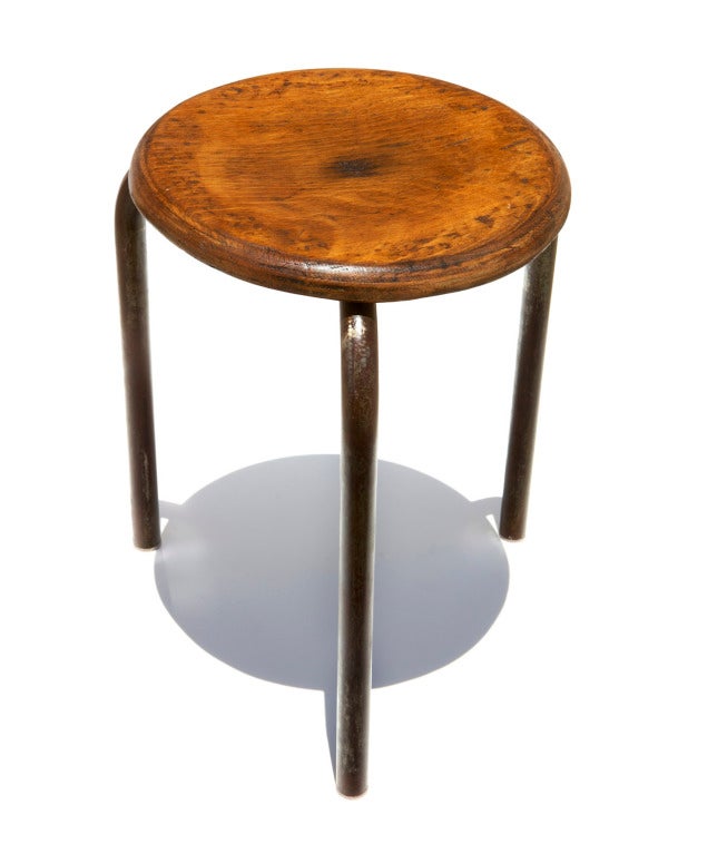 A simple tripod stool made by the Ateliers Jean Prouvé, with a slightly concave plywood seat and tubular steel legs. The base is formed by two tubes that are joined in a kind of 