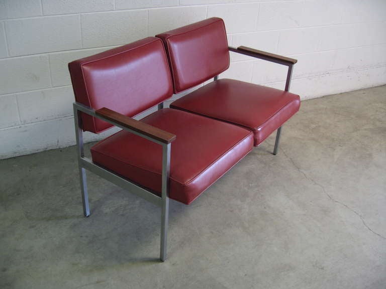 Superb Steelcase two seater settee or love seat, dating to 1960. 

Rendered in brushed stainless steel, this piece is rare to find as a dual unit.  Armrests are maple, vinyl is original and in a deep coral color.

Small pin hole on the fascia