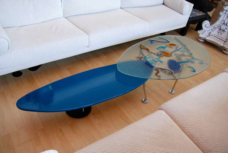 Wonderful! Two part, bi-level Saporiti Italia coffee table.The glass table measures two inches higher than the elongated solid blue enameled steel surfboard shaped  table. The glass table has wonderful abstract colorful applied glass design to top