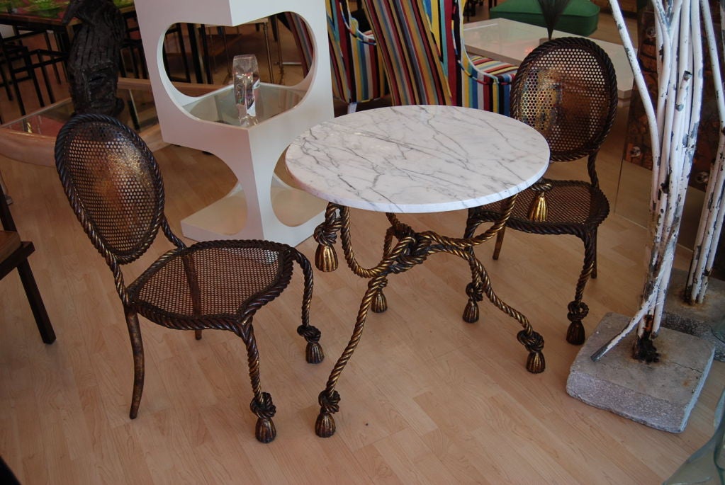 Chic Dorothy Draper pair of chairs with guilded rope and tassels.Great matching marble top table.Beautiful patina with undertones of rouge.Chairs are solid and substantial.Perfect for any room!Table dimensions:29 H x 26