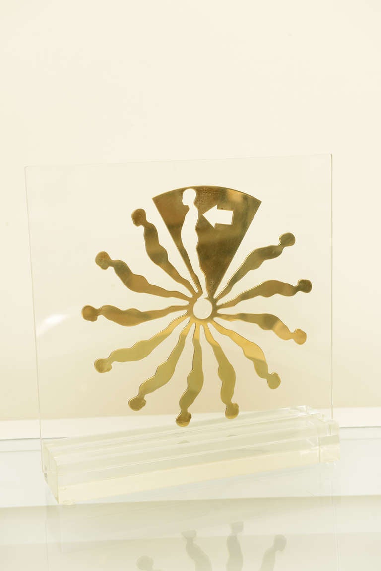 The famous falling man motif of Ernest Trova's sculpture is made of brass attached to the Lucite backing that slides into the Lucite base. It is a limited edition series that is signed and numbered. This is numbered 51/175. This was done in 1969. It