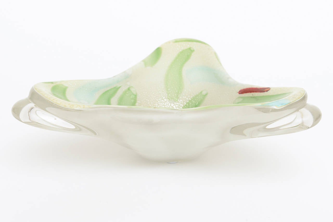 The beautiful Italian Murano glass bowl has brush like strokes of subtle colors of jade green, light blue and red streak is offset with inclusion of silver foil that glisten.
The shape of the bowl is sculptural. The outside appendages are clear and