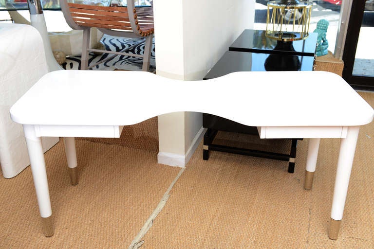 This white lacquered cork top that cinches in the middle of the
desk /vanity has 2 small pull out drawers The tapered legs are also white lacquered over wood and the cuffs are nickel silver. The center pinched in sides measure 12