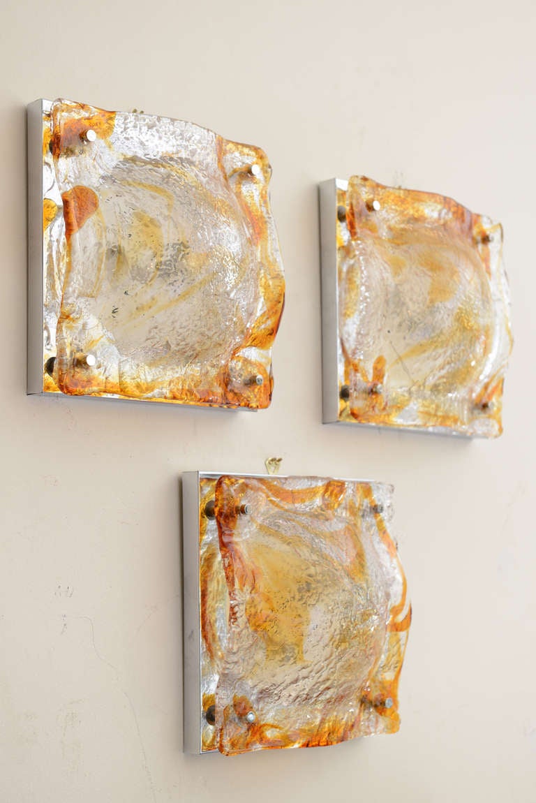 These amazing and beautiful set of six vintage Italian sculptural wall sconces of Murano glass by Mazzega have fused amber, orange and clear glass fronts put together with chrome pins and backing. The glass has a bowed bent to it. The collection of