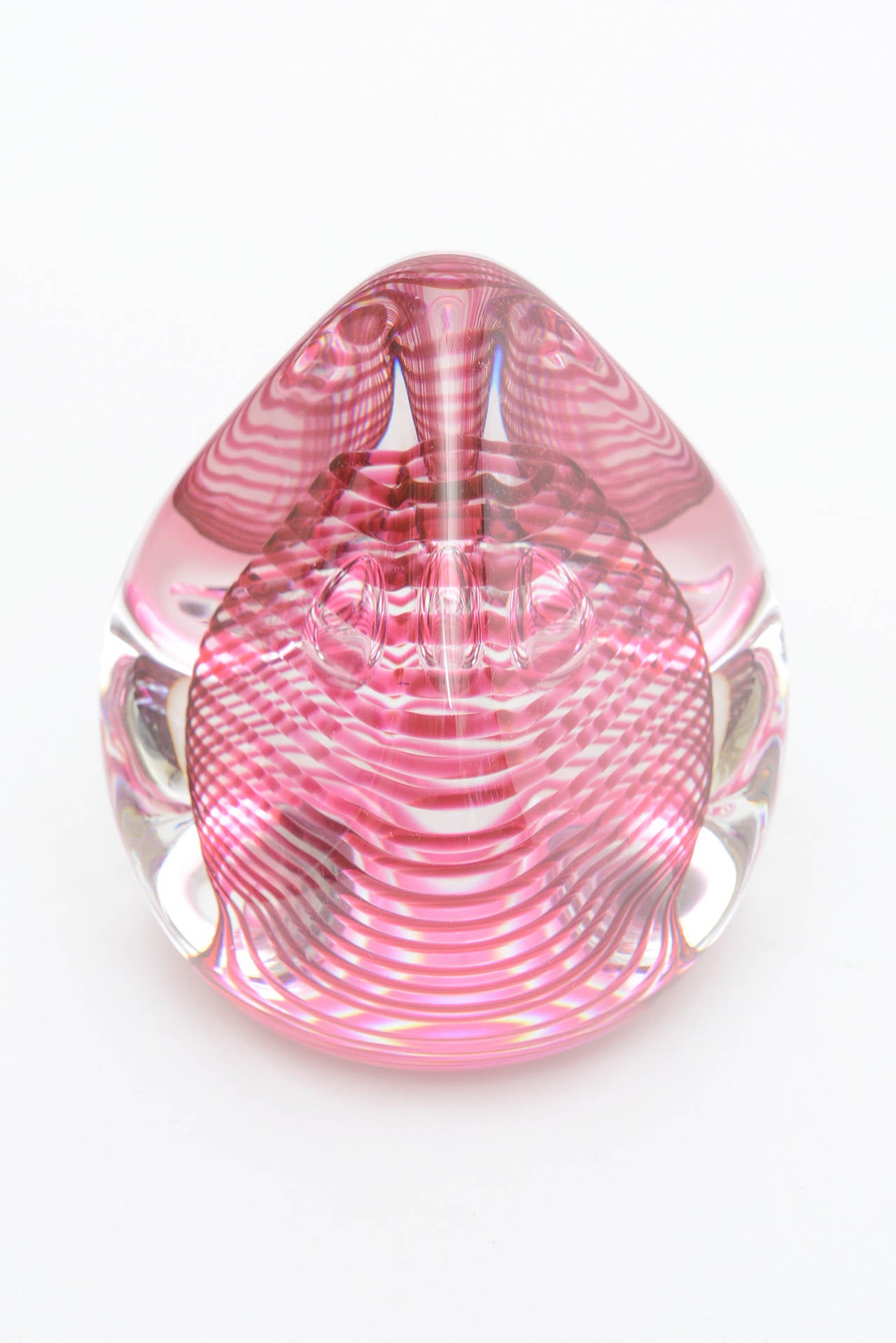 This gorgeous Swedish glass paperweight and or object looks like a teardrop or a kiss candy. Luscious bands of magenta pink swirl in spiral form incased in clear glass there are three floating teardrop bubbles inside the spirals. This is from Studio