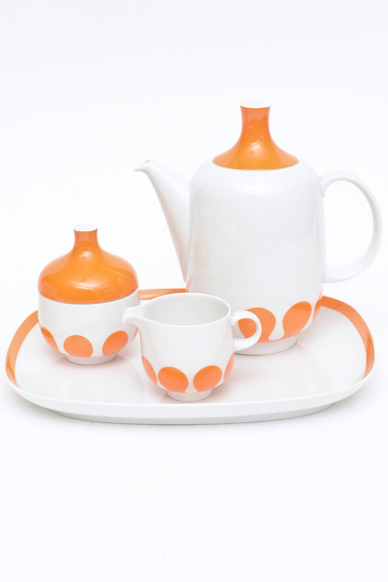 The pop of orange and white in this early 1960s very mod five-piece Rosenthal china service consists of a big serving bowl, a tray, coffee or tea, creamer and sugar.
The orange exaggerated teardrop bubble designs that surrounds the base of each