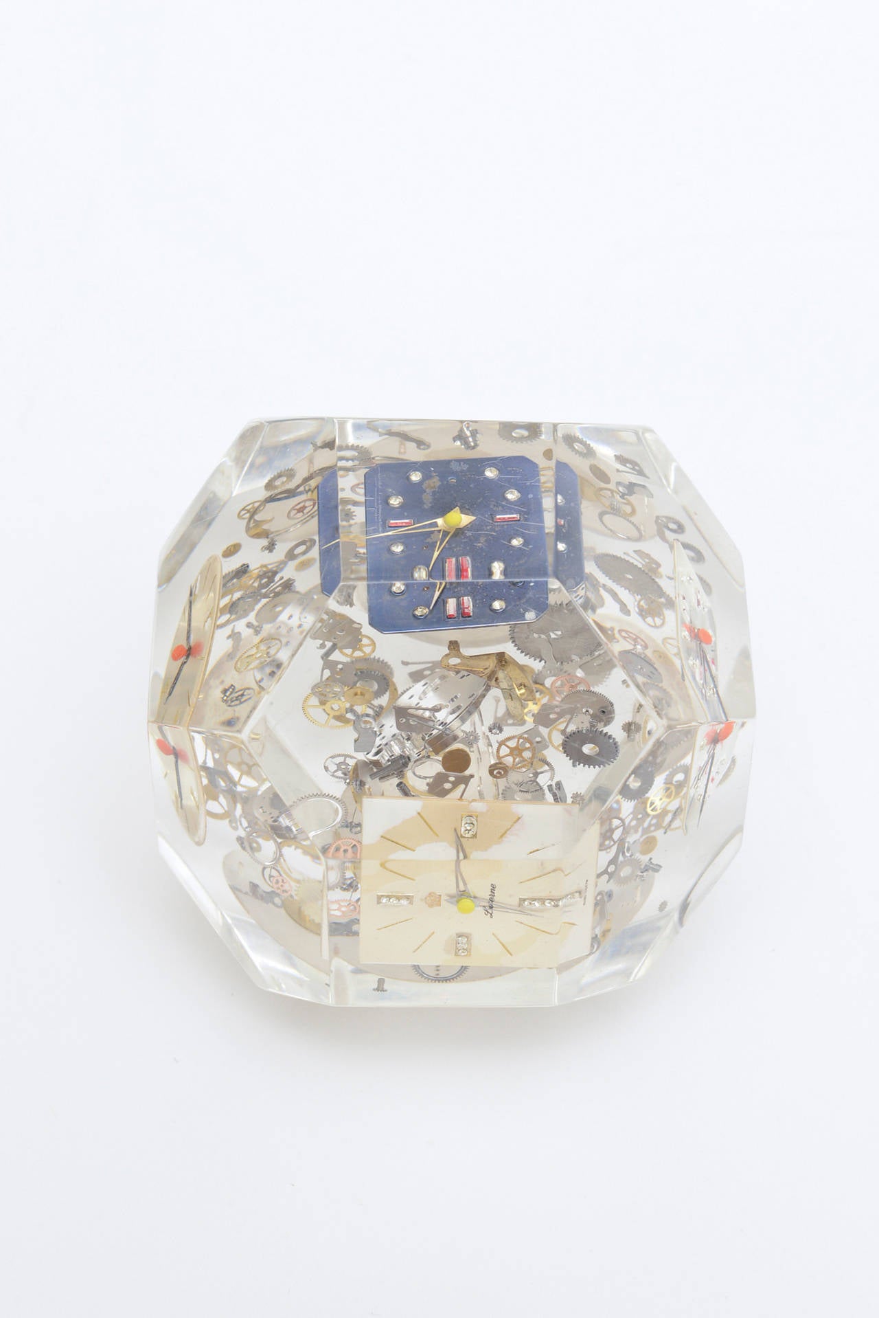 Hundreds of tiny Lucite watch parts and face clocks are embedded in this amusing and artful sculptural faceted Lucite paperweight.
It has the influence and style of the famous artist: Arman. This has a lot of work to it.
A great fun and