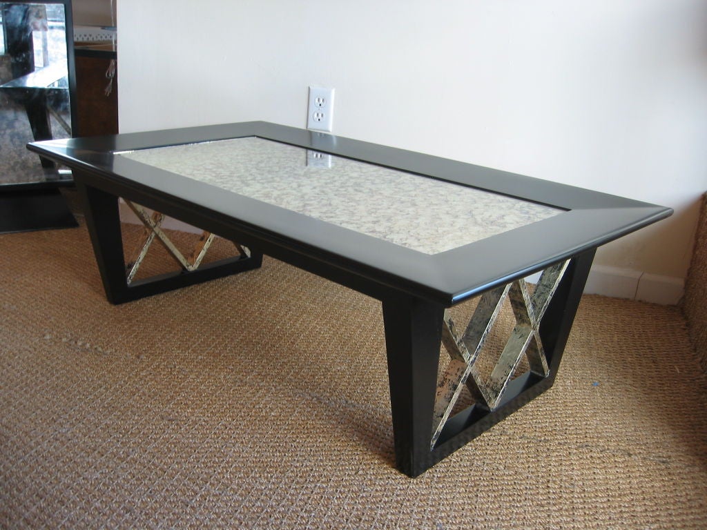  This wonderful vintage cocktail table finished in black satin with inverted X frame rubbed gold leafed legs. A golden eglomise mirrored top plays off the black body and the silver leafed legs. Please note: it is now not in perfect restored