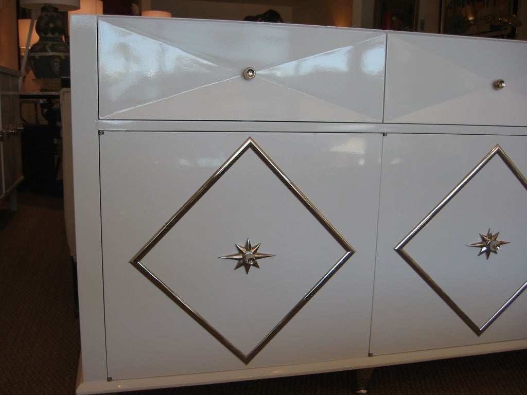 Elegant high gloss white lacquered dresser with original nickel silvered diamond design and starburst door pulls. Three doors reveal two large drawers, each with nautical recessed nickel silvered hoop pulls. Top drawers are concave and shaped with a