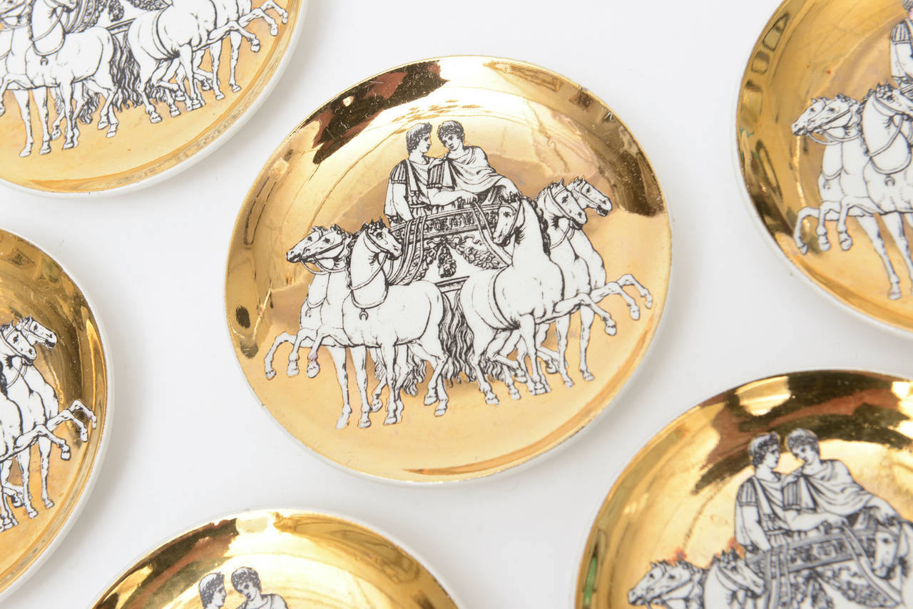 Rich in subject matter and rich in gold porcelain are these lovely Fornasetti complete set of eight Roman Chariot coasters. They have a romantic quality to them. The top is rich in gilded porcelain. The coasters feature a Roman Male/female with