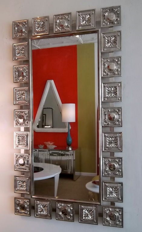 This fabulous Mid-Century Modern heavy textural mirror features alternate squares of two different raised designs. A Fleur de Lis meets a repeating circle that is attached and joined by a flat metal stretcher. It has recently been polished and